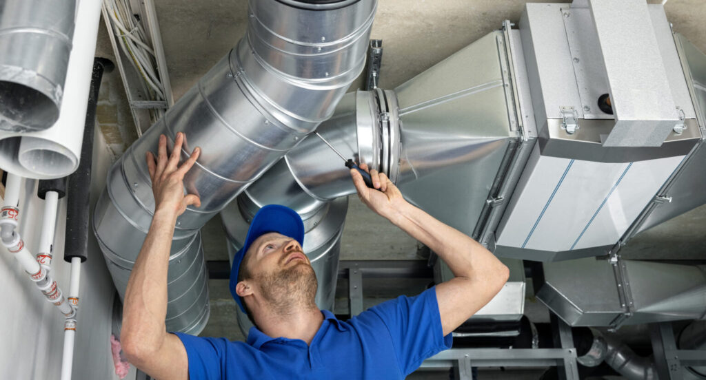 A technician in a blue cap and t-shirt fixing an air duct