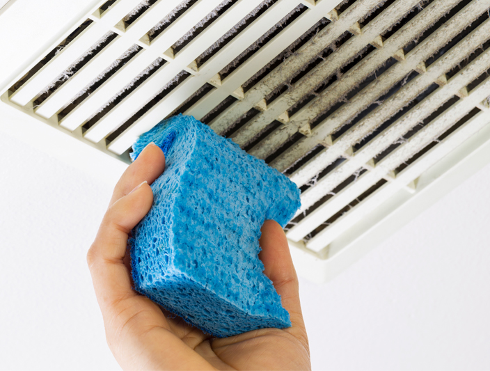 a hand holding a blue sponge to clean a vent